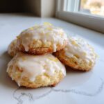 A stack of soft, glazed lemon cookies topped with bright yellow lemon zest.