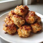 A pile of freshly baked, golden brown bisquick sausage balls stacked on a white plate.