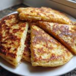 A stack of freshly cooked, golden brown irish potato farls, some cut into wedges, served on a white plate.
