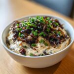 Close-up of a creamy onion dip topped generously with caramelized onions and fresh green chives.