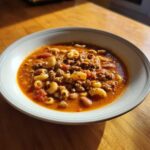 Close-up of a bowl of rich, tomato-based pasta e fagioli soup with ground meat, small pasta shapes, and beans.
