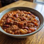 Close-up of a rustic bowl filled with rich, tomato-based pasta e fagioli soup featuring ground meat, kidney beans, and small pasta shapes.