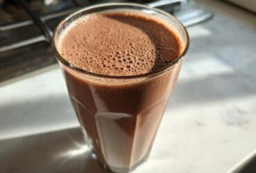 A tall glass filled with freshly made chocolate milk, showing a layer of small foam bubbles on top.