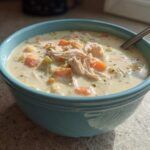 A close-up of a blue bowl filled with homemade cream of chicken soup, featuring shredded chicken and diced carrots.