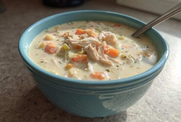 A close-up of a blue bowl filled with homemade cream of chicken soup, featuring shredded chicken and diced carrots.