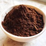 A white bowl filled high with rich, dark brown homemade hot cocoa mix powder.
