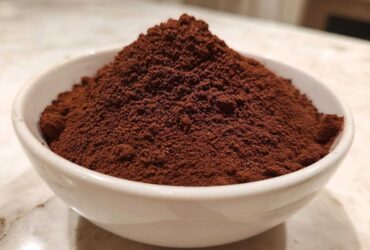 Close-up of a generous mound of rich, dark brown homemade hot cocoa mix powder overflowing a small white bowl.