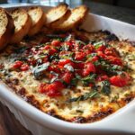 Close-up of hot baked bruschetta dip topped with diced tomatoes and basil, served with toasted baguette slices.
