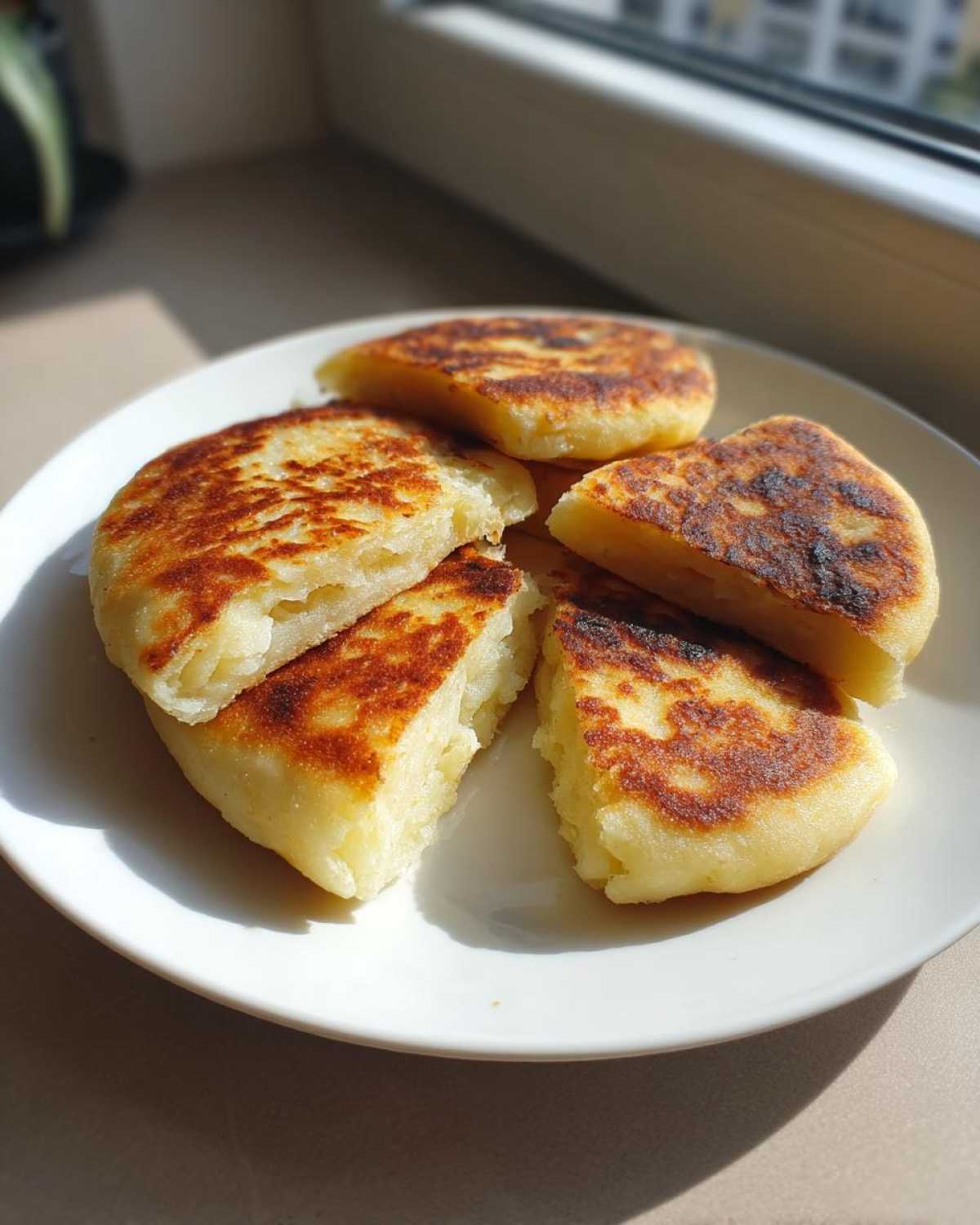 Close-up of several golden-brown Irish potato farls stacked on a white plate, beautifully browned from frying.