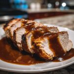 Close-up of sliced crockpot turkey breast covered in rich brown gravy on a white plate.