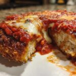 Close-up of keto chicken parmesan cut in half, showing crispy breading, white chicken interior, marinara sauce, and melted mozzarella cheese.