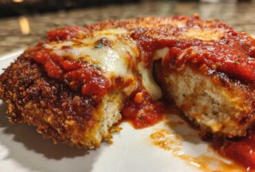 Close-up of keto chicken parmesan cut in half, showing crispy breading, white chicken interior, marinara sauce, and melted mozzarella cheese.