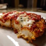 A close-up cross-section of a juicy keto chicken parmesan serving, topped with melted mozzarella and marinara sauce.