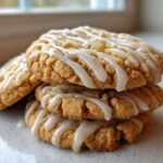 A stack of three soft maple brown sugar cookies drizzled with a thick, white glaze, sitting on a light countertop.