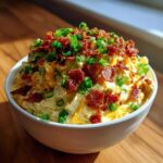 A creamy bowl of Million Dollar Dip topped generously with crumbled bacon and fresh green onions.