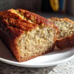 A close-up of a moist banana bread loaf with one slice cut, showing the tender crumb texture.
