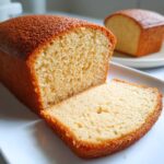 Close-up of a moist, golden-brown slice cut from a loaf of condensed milk cake on a white plate.