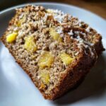Close-up of a moist slice of hawaiian banana bread studded with pineapple chunks and topped with shredded coconut.
