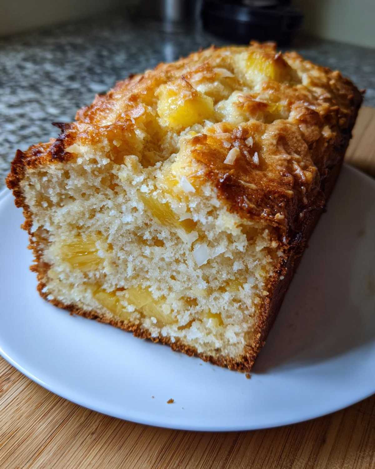 Close-up of a slice of moist hawaiian banana bread studded with chunks of pineapple and topped with toasted coconut.