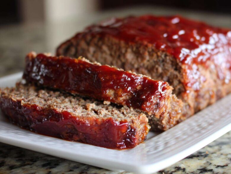 Close-up of a moist meatloaf, sliced and covered in a shiny, thick red glaze.