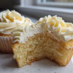 Close-up of a vanilla cupcake cut in half showing the moist crumb texture and rich vanilla frosting.