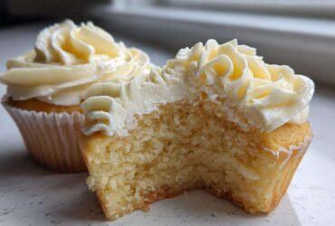 Close-up of a vanilla cupcake cut in half showing the moist crumb texture and rich vanilla frosting.