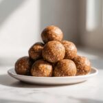 A pyramid stack of homemade, no-bake protein balls with visible seeds, served on a small white plate.