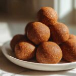 A stack of golden brown, textured no-bake protein balls piled high on a white plate.