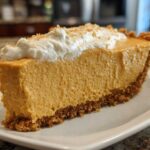 Close-up of a thick slice of creamy no bake pumpkin pie on a white plate, topped with whipped cream.