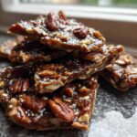 A stack of shiny, broken pieces of homemade Pecan Pie Bark, rich with pecans and caramel glaze.