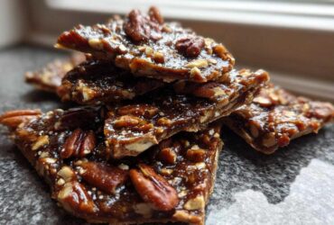 A stack of shiny, broken pieces of homemade Pecan Pie Bark, rich with pecans and caramel glaze.