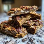 Close-up of a stack of homemade Pecan Pie Bark squares topped with whole pecans on a granite counter.