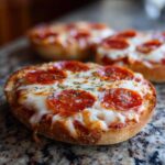 A close-up of a freshly baked pepperoni english muffin pizza topped with melted mozzarella and herbs.