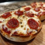 Close-up of a freshly baked pepperoni english muffin pizza topped with melted cheese and herbs.