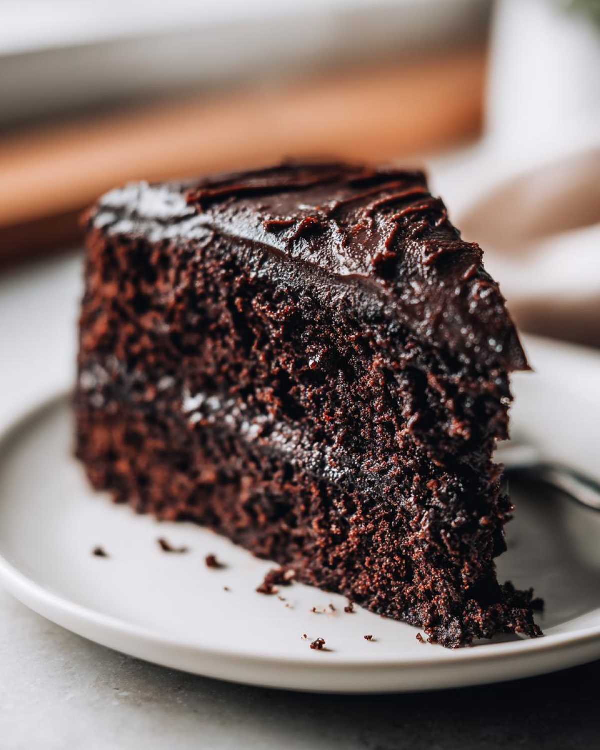 Close-up of a moist slice of dark chocolate fudge cake topped with glossy chocolate frosting.