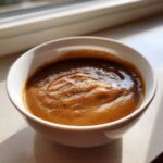 A close-up of rich, brown turkey gravy seasoned with cracked black pepper in a small white bowl.