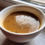 Close-up of rich, brown turkey gravy seasoned with black pepper in a small white bowl.