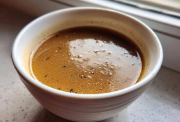 Close-up of rich, brown turkey gravy seasoned with black pepper in a small white bowl.