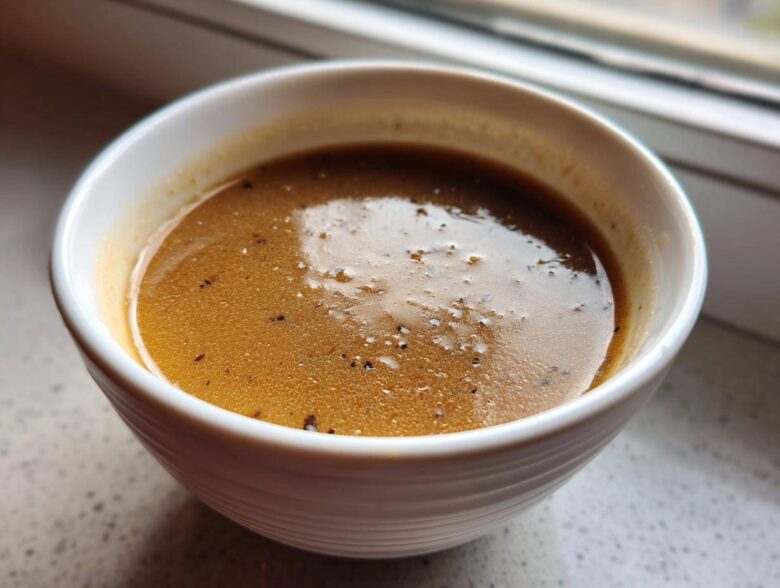 Close-up of rich, brown turkey gravy seasoned with black pepper in a small white bowl.