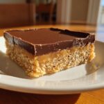 A single square of three-layer lunch lady peanut butter bars with a crumbly base, caramel layer, and chocolate topping.
