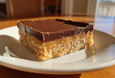 A single square of three-layer lunch lady peanut butter bars with a crumbly base, caramel layer, and chocolate topping.