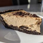 A close-up slice of amazing peanut butter pie featuring a thick, creamy filling and a dark chocolate crumb crust.