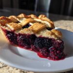 A delicious slice of blackberry pie featuring a thick, juicy filling and a golden lattice crust, sitting on a white plate.