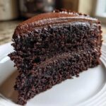 Close-up of a rich, dark slice of homemade chocolate cake layered and topped with glossy chocolate frosting.