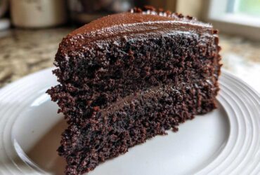 Close-up of a rich, dark slice of homemade chocolate cake layered and topped with glossy chocolate frosting.