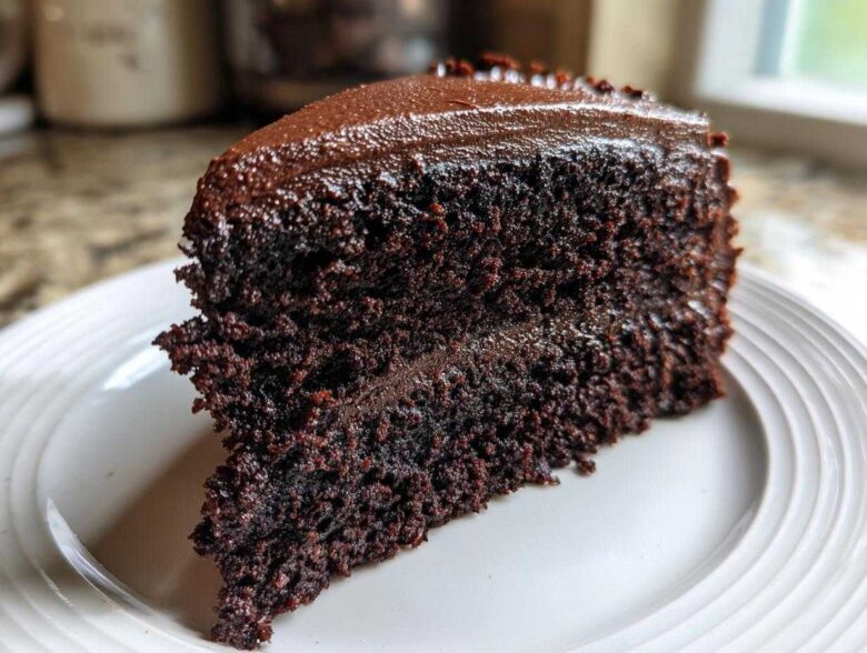 Close-up of a rich, dark slice of homemade chocolate cake layered and topped with glossy chocolate frosting.
