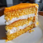 A tall slice of Creamsicle Cake showing three layers of orange sponge cake separated by thick white cream filling.