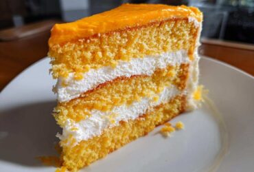 A tall slice of Creamsicle Cake showing three layers of orange sponge cake separated by thick white cream filling.