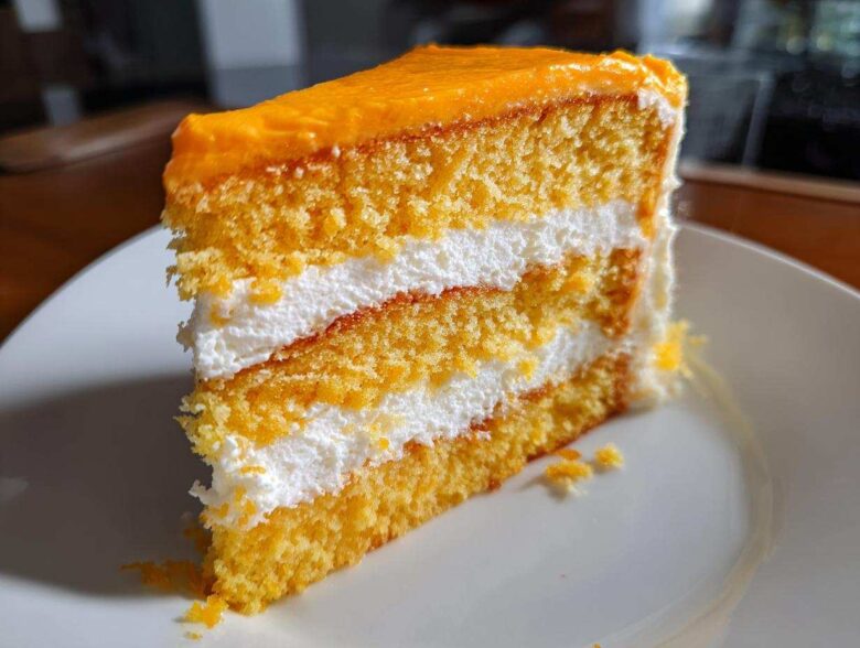 A tall slice of Creamsicle Cake showing three layers of orange sponge cake separated by thick white cream filling.