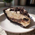 A close-up slice of creamy peanut butter pie featuring a dark chocolate crust and topped with crushed cookies.